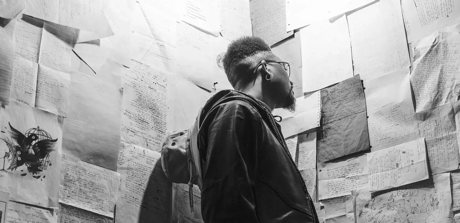 Ellis Ricketts in a cap and jacket, looking up at a wall covered in his sketches